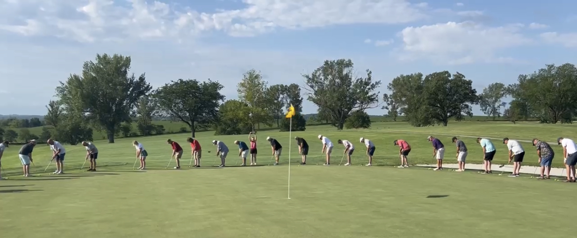 a long line of people about to take a shot at the golf green flag in the middle of the picture