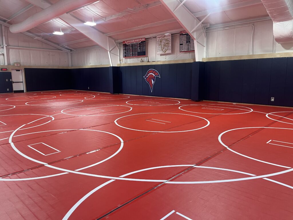 wresting room with a room full of red wresting mats and a big trojan head logo on the wall